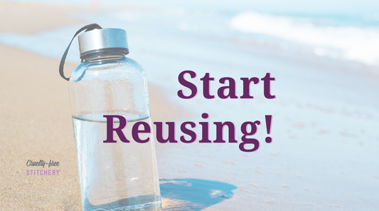 Start reusing! A photo of a glass water bottle stuck in the sand near the shore of a pristine beach.