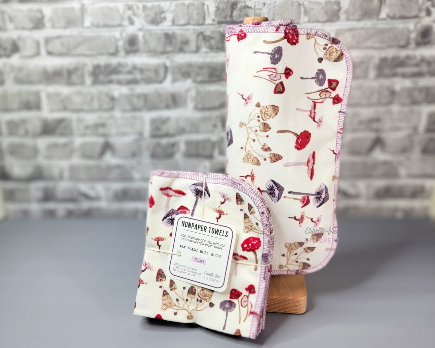 Mushrooms print NonPaper Towels - a slightly off-white with smallwild mushrooms in reds, purples, and browns. Shown as a bundled pack next to some rolled on a wooden paper towel holder.