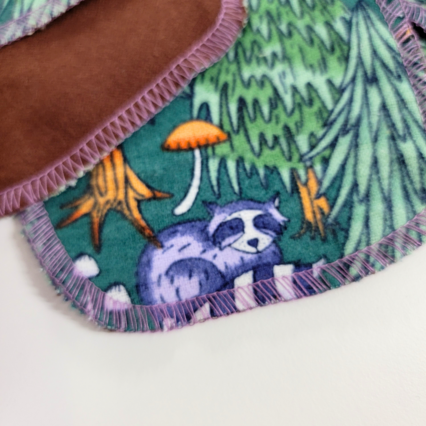Close-up of a cotton round with a raccoon on it, and part of the back of another that is dark brown.