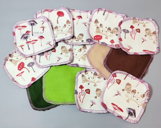 Mushrooms print reusable cotton rounds, scattered around with some upside down to show the backs have dark forest green, light bud green, tan, and dark brown. They are rounded squares.