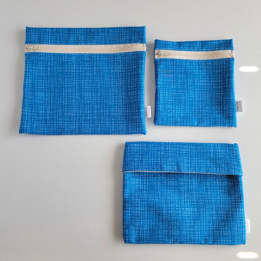 Three Blue Texture Reusable Snack Bags arranged separately to show the difference between sizes. Large Zip is not quite double the size of the Small Zip, and the Foldover is slightly smaller than the Large Zip.
