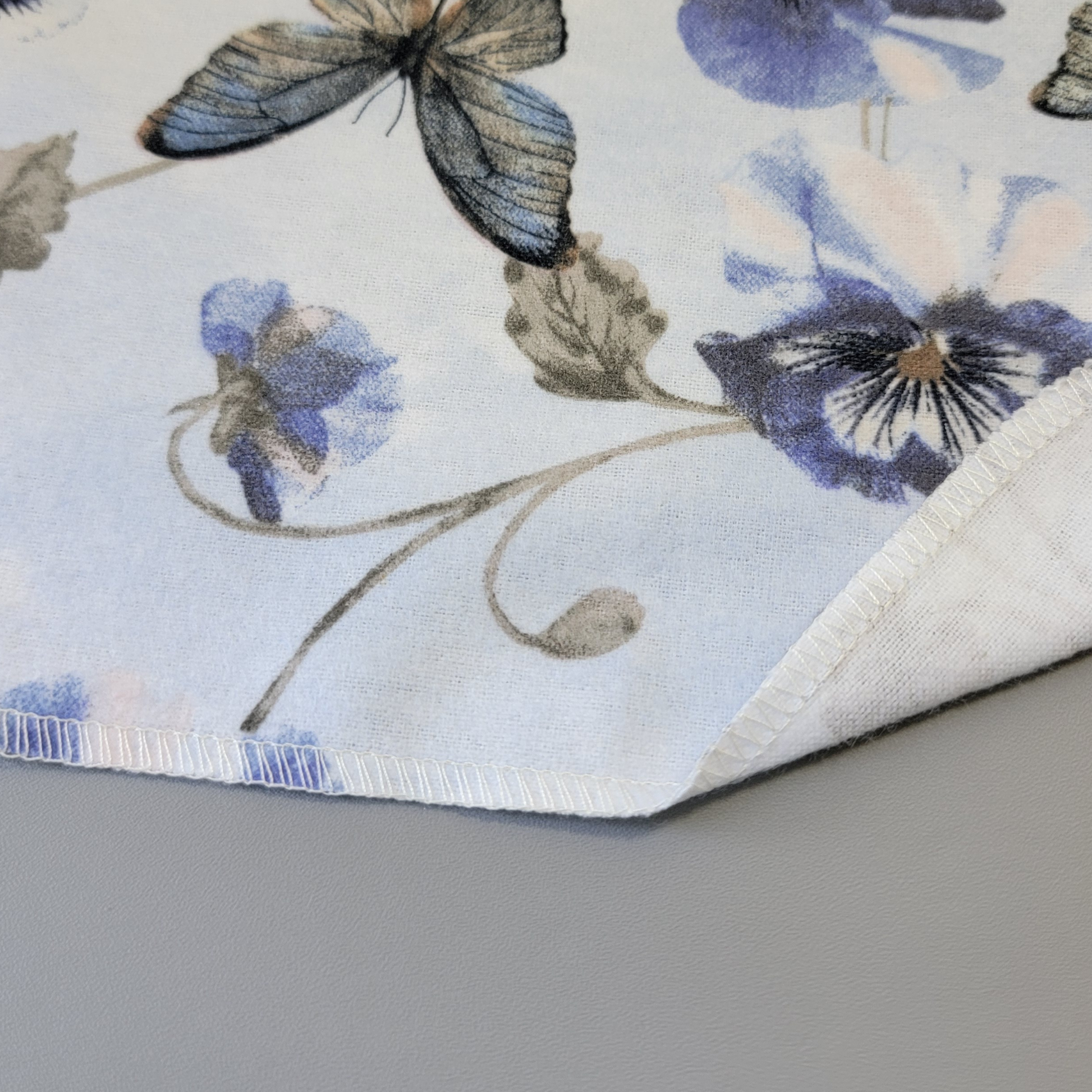 The bottom edge of a Butterfly Violet NonPaper Towel close-up to show the detail of the stitching. The edge is partially folded back to show the back side is unprinted, and there is one layer of material.