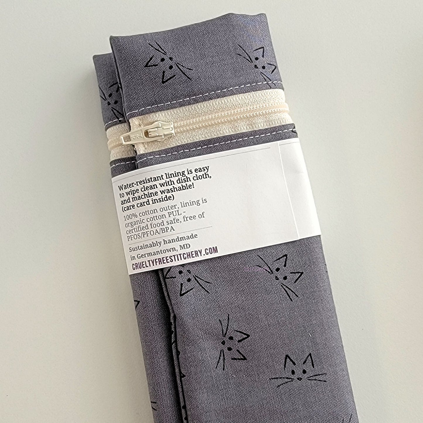 The back of the Snack Bag packaging. It says "Water resistant lining is easy to wipe clean with dish cloth, and machine washable. Care card inside. 100% cotton outer, lining is organic cotton PUL, cerfitied food-safe, free of PFOS, PFOA, BPA. Sustainable handmade in Germantown, MD" and our website url.