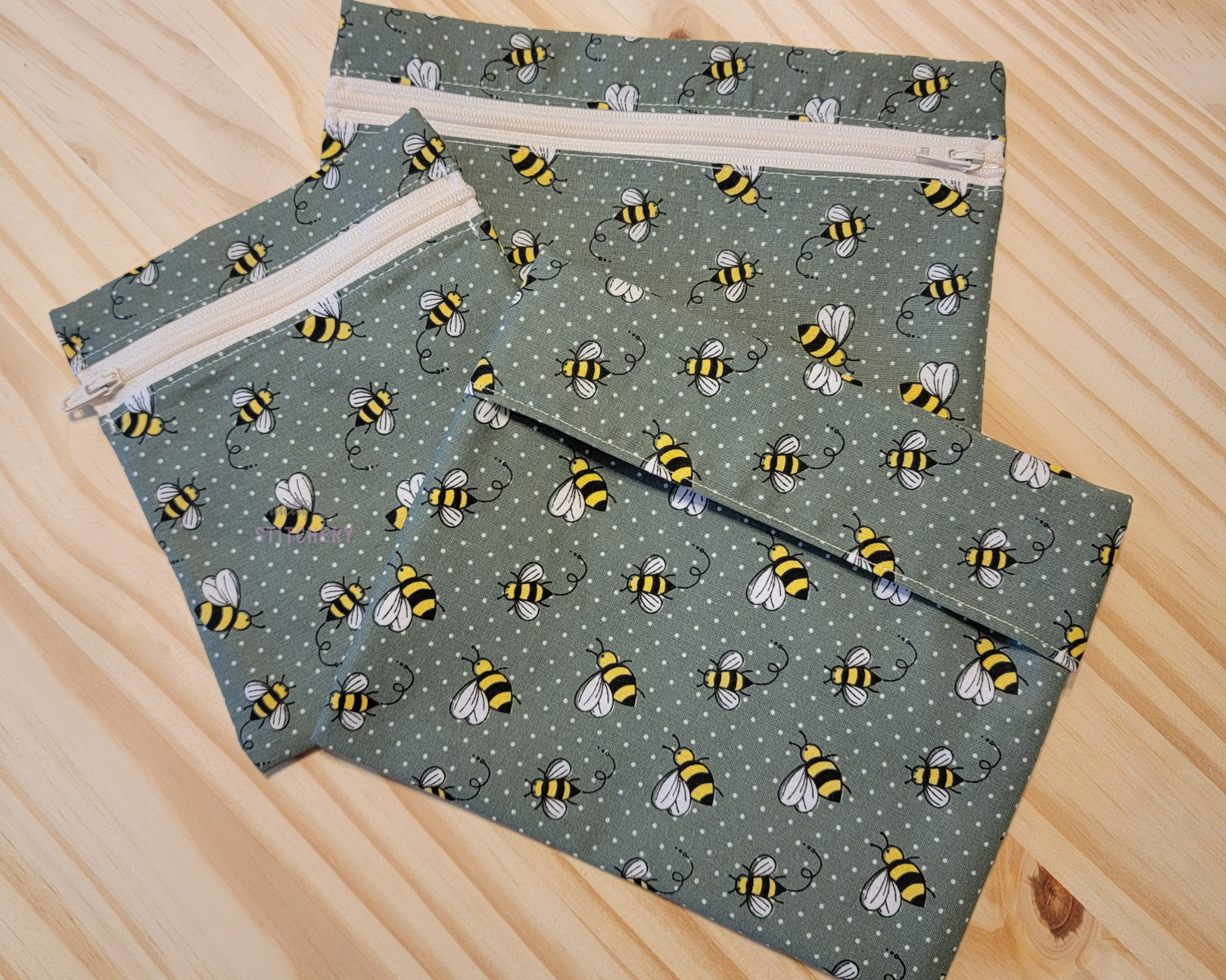 Three sizes of reusable snack bags in a sage green, tiny polka dots, and honey bees all over. Two sizes have zippers, which are an off-white color.
