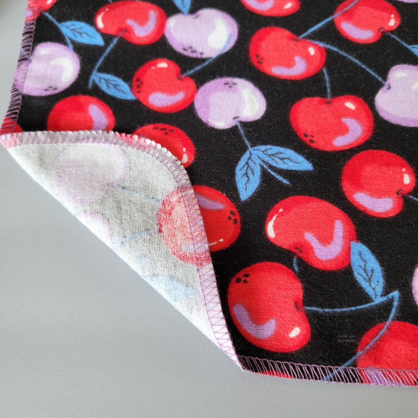 a close-up of the black cherries NonPaper Towel with the edge folded back to show the stitching, and that it is one layer with the back side unprinted white.