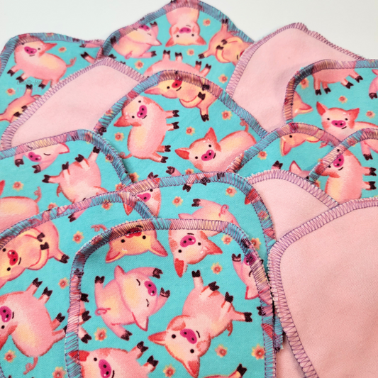 The blue with pigs cotton rounds arranged flat to show the pigs have various poses - sitting, laying down, etc. They have cute little brown hooves, and their noses are heart shaped.