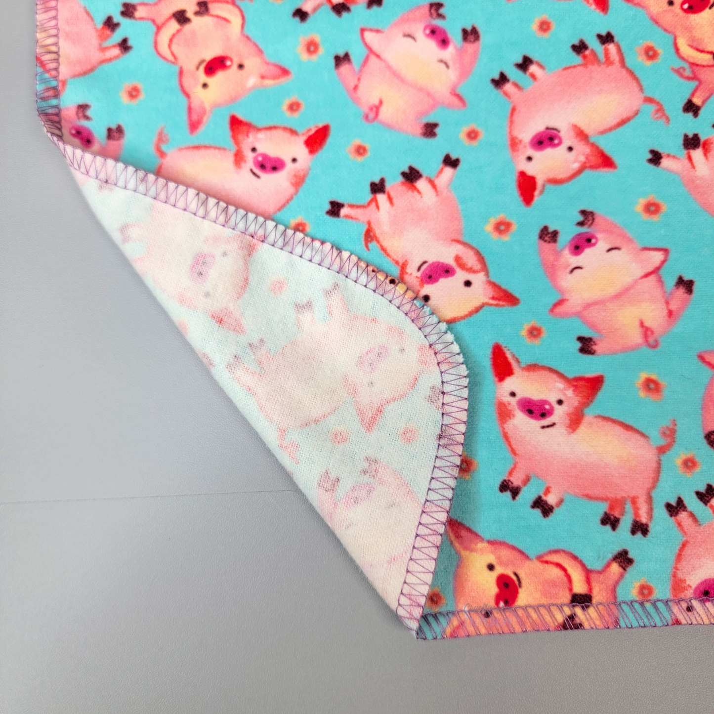 A close-up of the NonPaper Towel with the corner folded back to show that it is one layer, and printed on the front. The stitching is a light lilac purple color but it blends well with the pink and aqua blue colors.