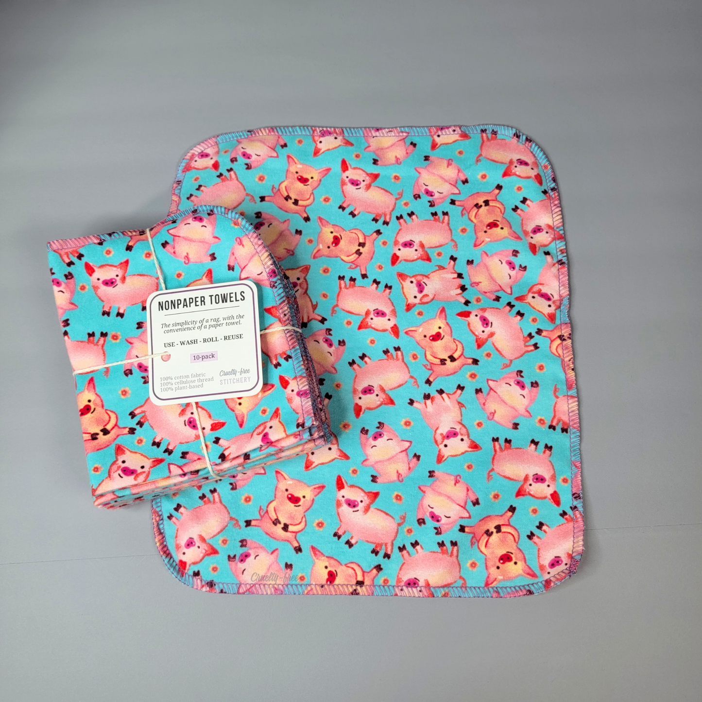 The blue pigs NonPaper towels - one opened and laid flat with the bundled pack on top. The bundled pack is a pack of 10, and the bundled ones are folded in half twice.