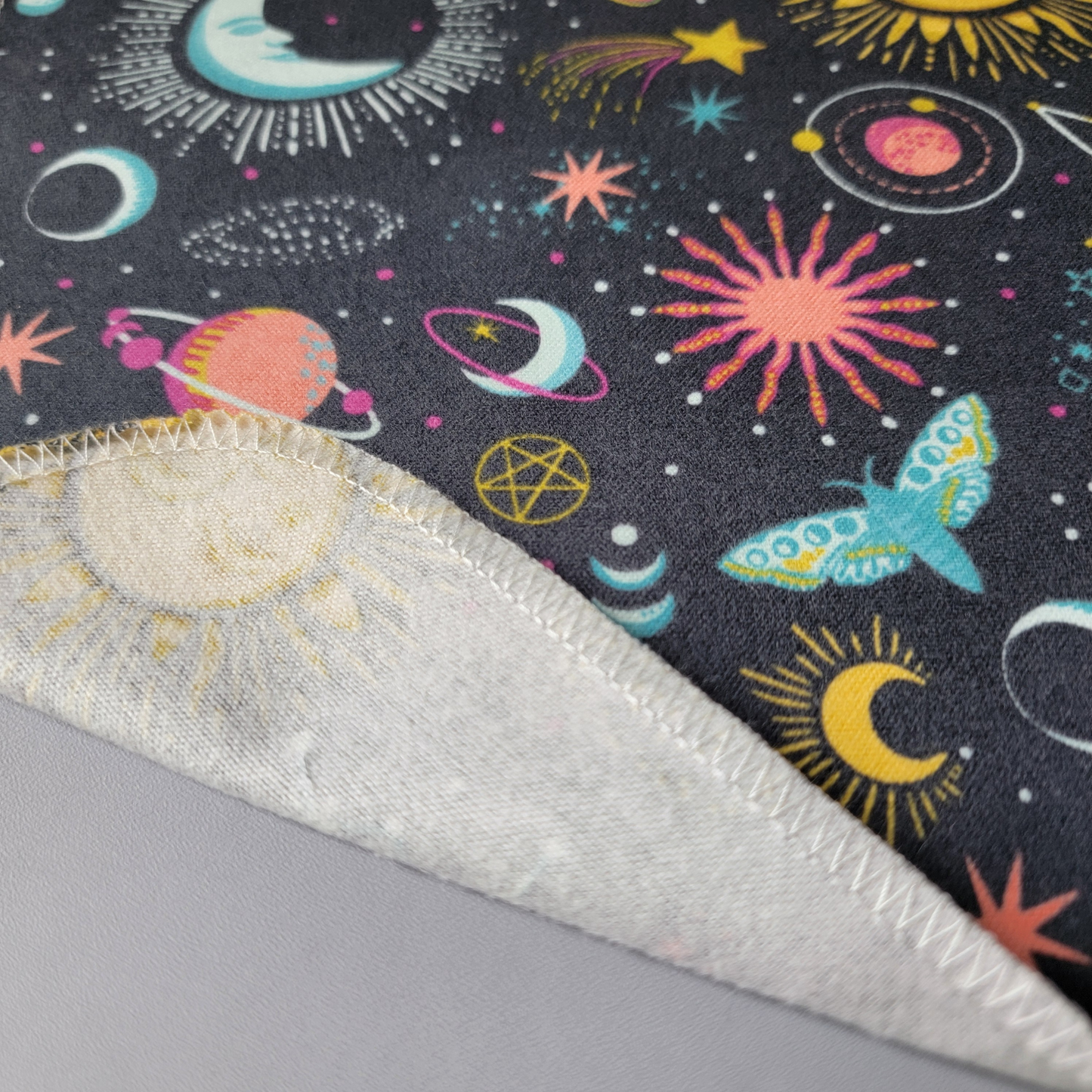 A close-up of a gray celestial nonpaper towel, with the edge folded back to show that they are one layer of fabric, and the back is unprinted white.