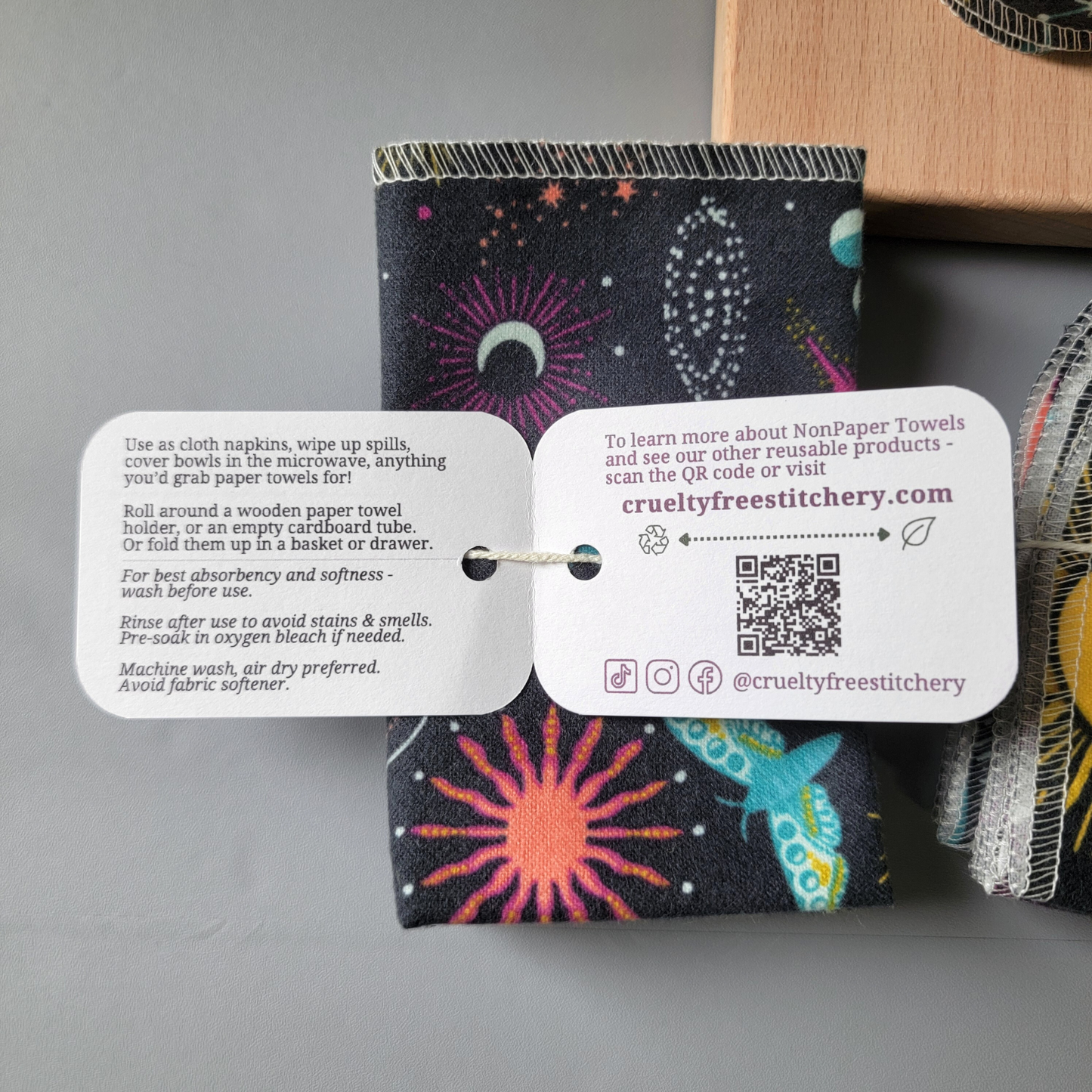Inside the tag of the gray celestial nonpaper towels, with care instructions and summary of description below. Other side has our website, a QR code, and social media handles @crueltyfreestitchery.