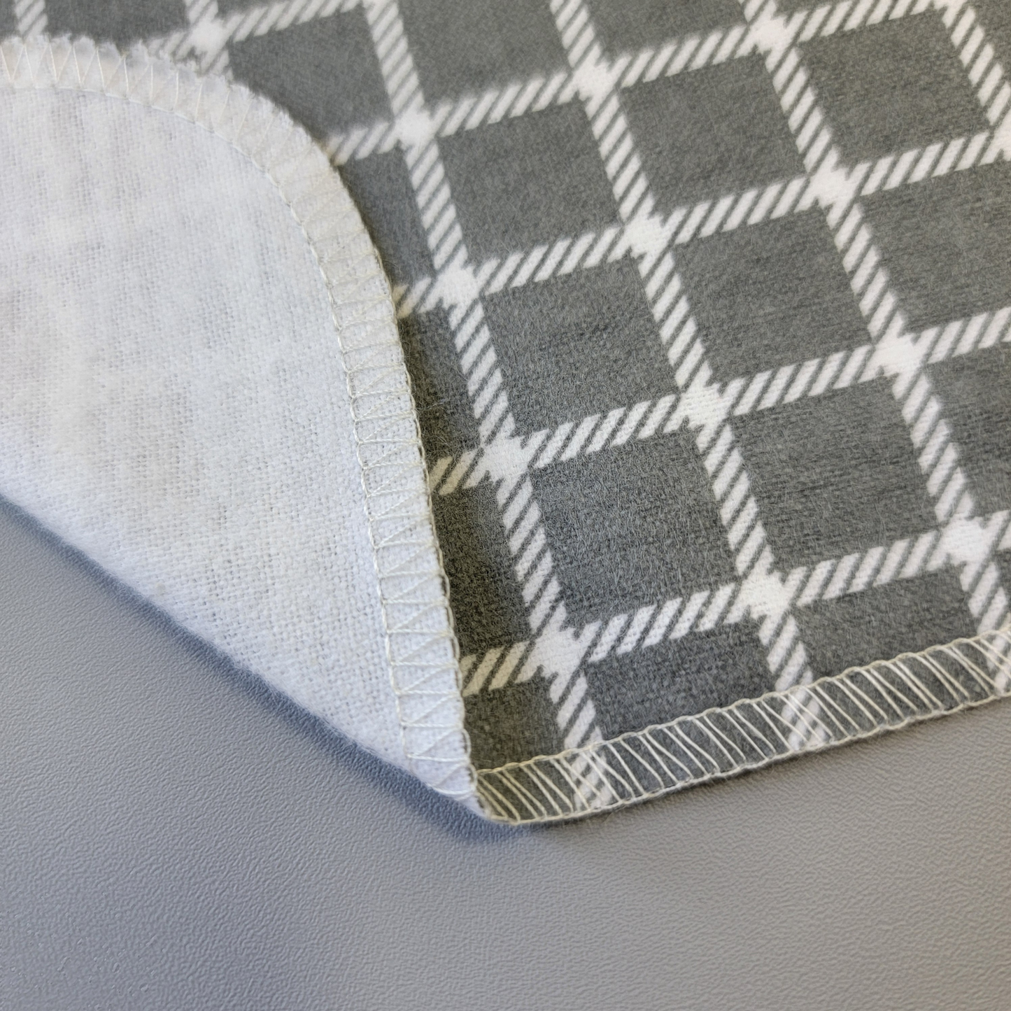 The bottom edge of a Gray Small Windowpane NonPaper Towel close-up to show the detail of the stitching. The edge is partially folded back to show the back side is unprinted, and there is one layer of material.