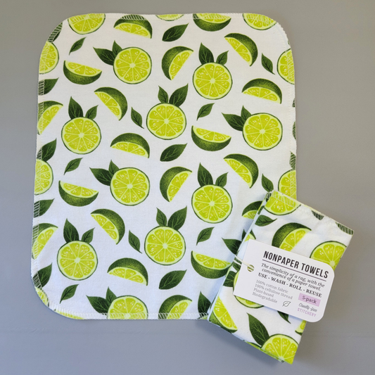 Limes print NonPaper Towel laid flat to show the detail of the print, with a bundled 5-pack sitting partially on top of it. The NonPaper Towel is a rectangular shape, with rounded corners, The edges are stitched in off-white thread. The bundle's tag says "NonPaper Towels, the simplicity of a rag with the convenience of a paper towel. Use, wash, roll, reuse. 100% cotton fabric, 100% cellulose thread. Plant based, biodegradable."