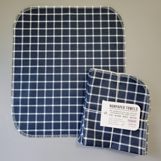 Navy Small Windowpane print NonPaper Towel laid flat to show the detail of the print, with a bundled 10-pack sitting partially on top of it. The NonPaper Towel is a rectangular shape, with rounded corners, The edges are stitched in off-white thread. The bundle's tag says "NonPaper Towels, the simplicity of a rag with the convenience of a paper towel. Use, wash, roll, reuse. 100% cotton fabric, 100% cellulose thread. Plant based, biodegradable."