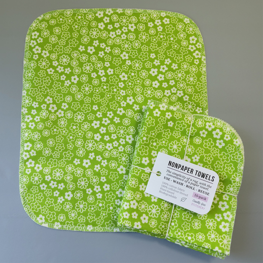 Retro Green Daisy print NonPaper Towel laid flat to show the detail of the print, with a bundled 10-pack sitting partially on top of it. The NonPaper Towel is a rectangular shape, with rounded corners, The edges are stitched in off-white thread. The bundle's tag says "NonPaper Towels, the simplicity of a rag with the convenience of a paper towel. Use, wash, roll, reuse. 100% cotton fabric, 100% cellulose thread. Plant based, biodegradable."