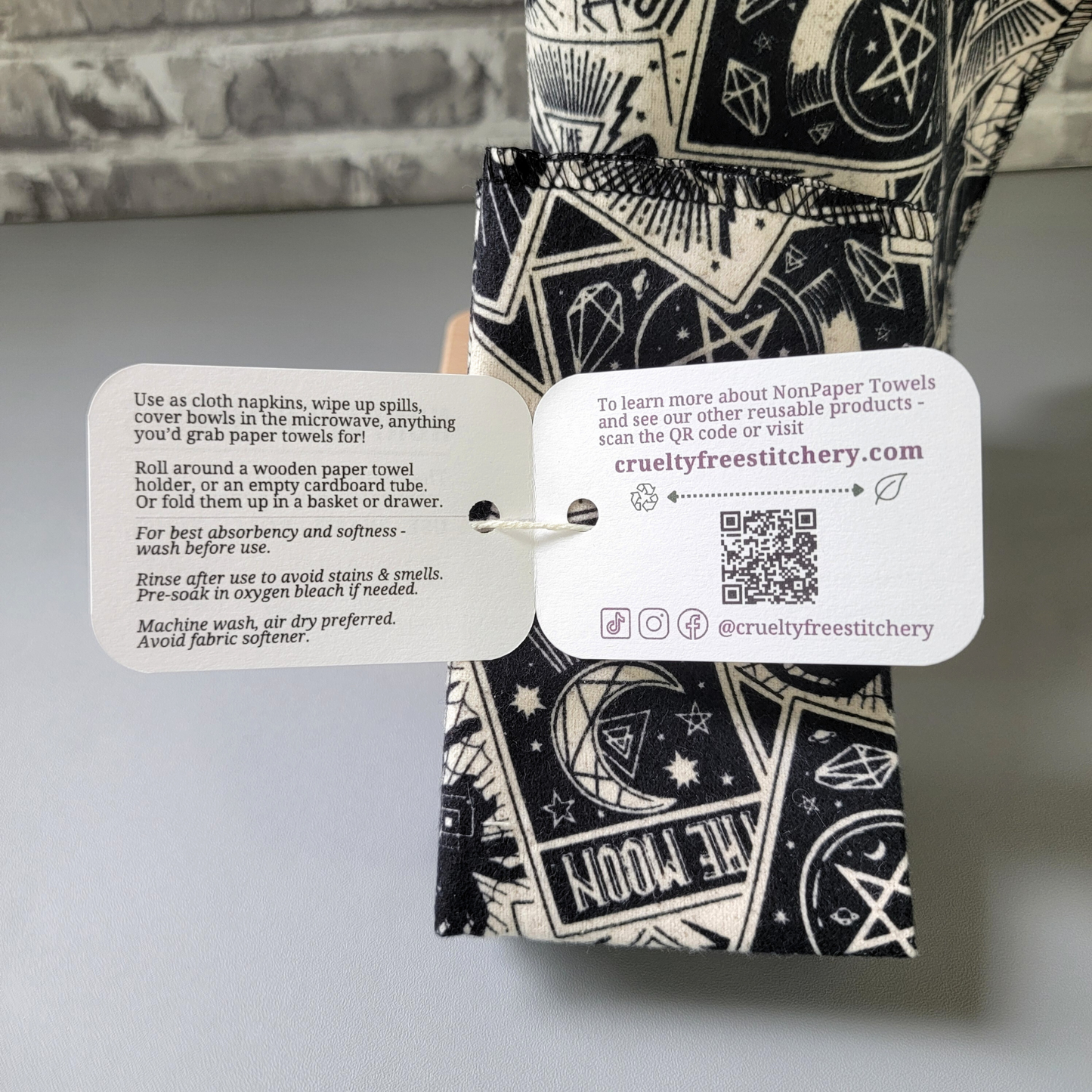 Inside the tag of the tarot card nonpaper towels, with care instructions and summary of description below. Other side has our website, a QR code, and social media handles @crueltyfreestitchery.