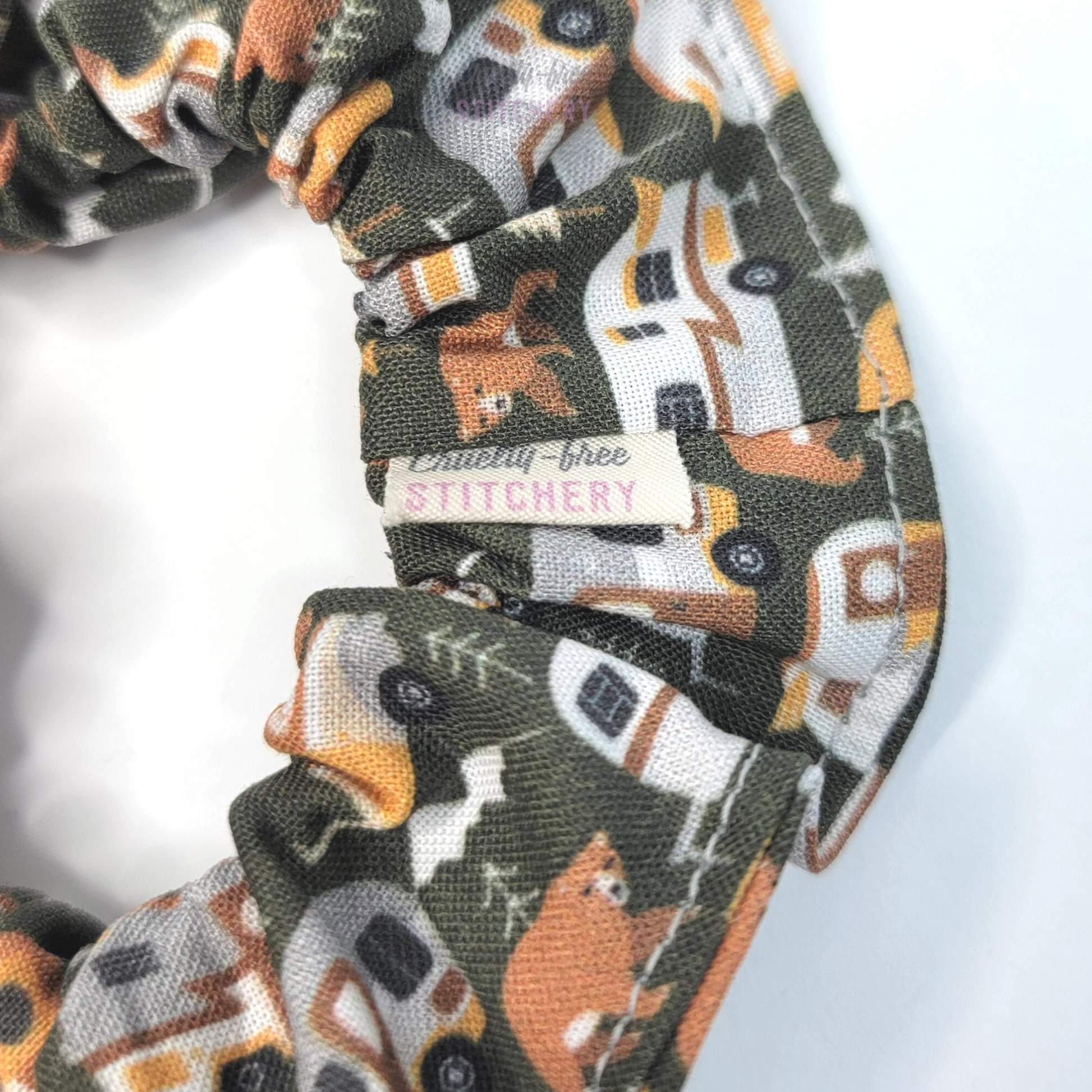 Close-up of the dark green scrunchie with bears, trees, and vintage campers. A small white tag has the Cruelty-Free Stitchery logo.