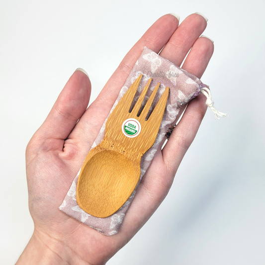 Mauve butterflies print fabric pouch with bamboo spork on top, laid on a hand for size reference. The spork is slightly longer than the fingers.