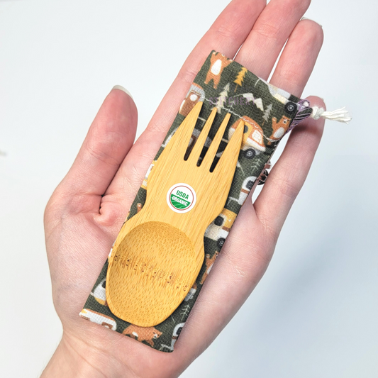 Dark green vintage campers print fabric pouch with bamboo spork on top, laid on a hand for size reference. The spork is slightly longer than the fingers.