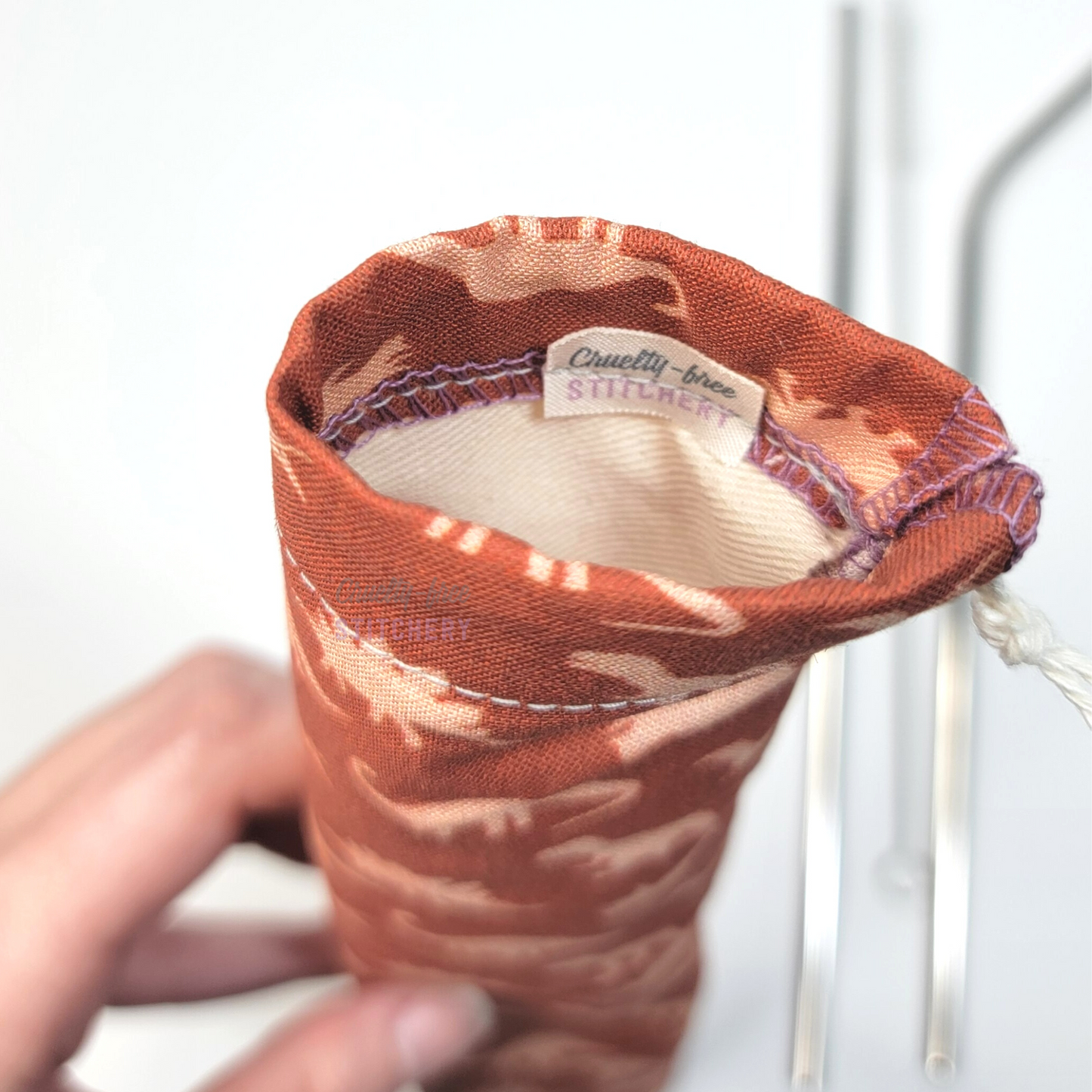 Reusable straw pouch viewed from the top down to show the inside. There is a tiny white tag with the Cruelty-Free Stitchery logo, and a natural-color lining.