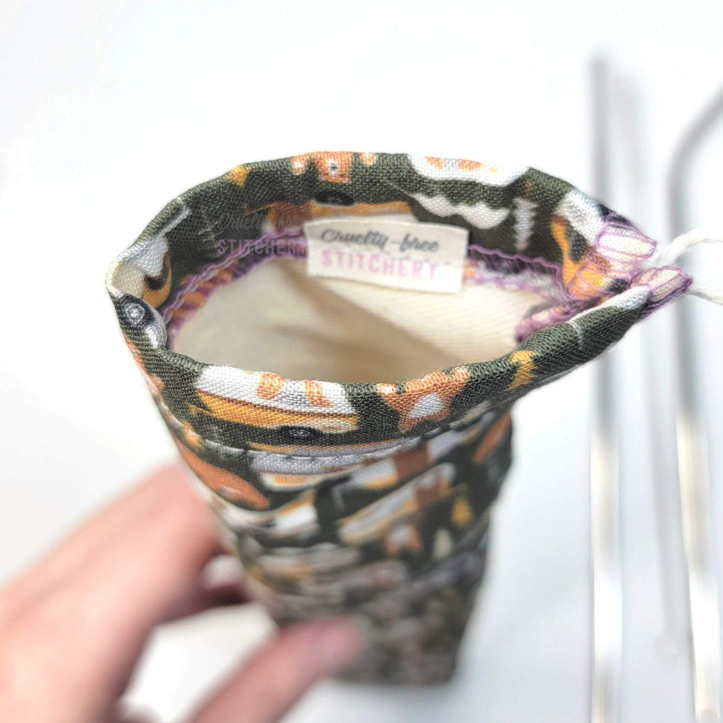 Reusable straw pouch viewed from the top down to show the inside. There is a tiny white tag with the Cruelty-Free Stitchery logo, and a natural-color lining.