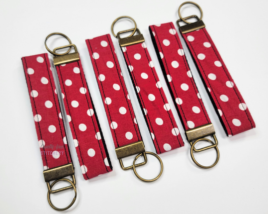 Key fob wristlets, the straps are red with white polka dots and they have antiqued brass hardware and key ring. Photo arranged with six of them in alternating directions.