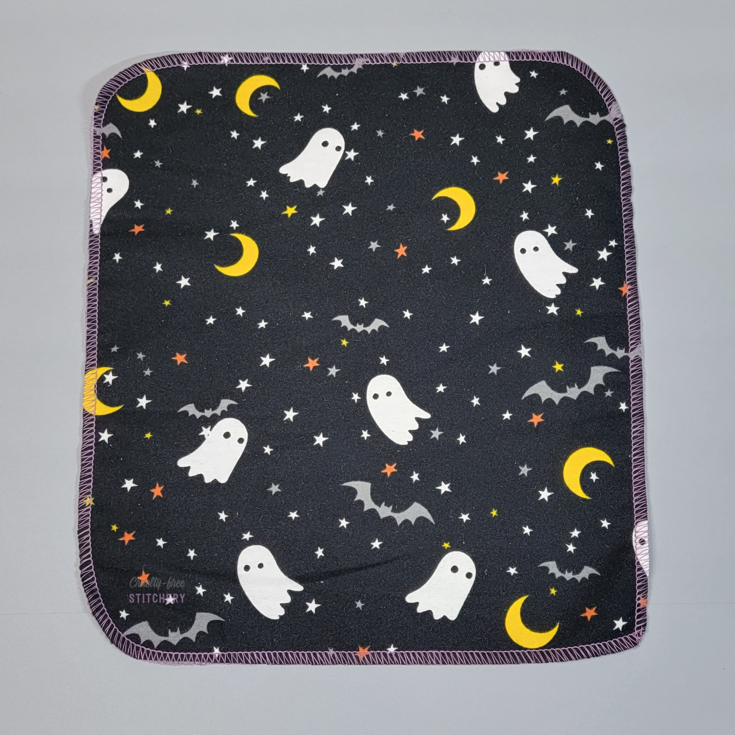 A black NonPaper Towel printed with white ghosts, grey bats, yellow crescent moons, and white and orange stars.