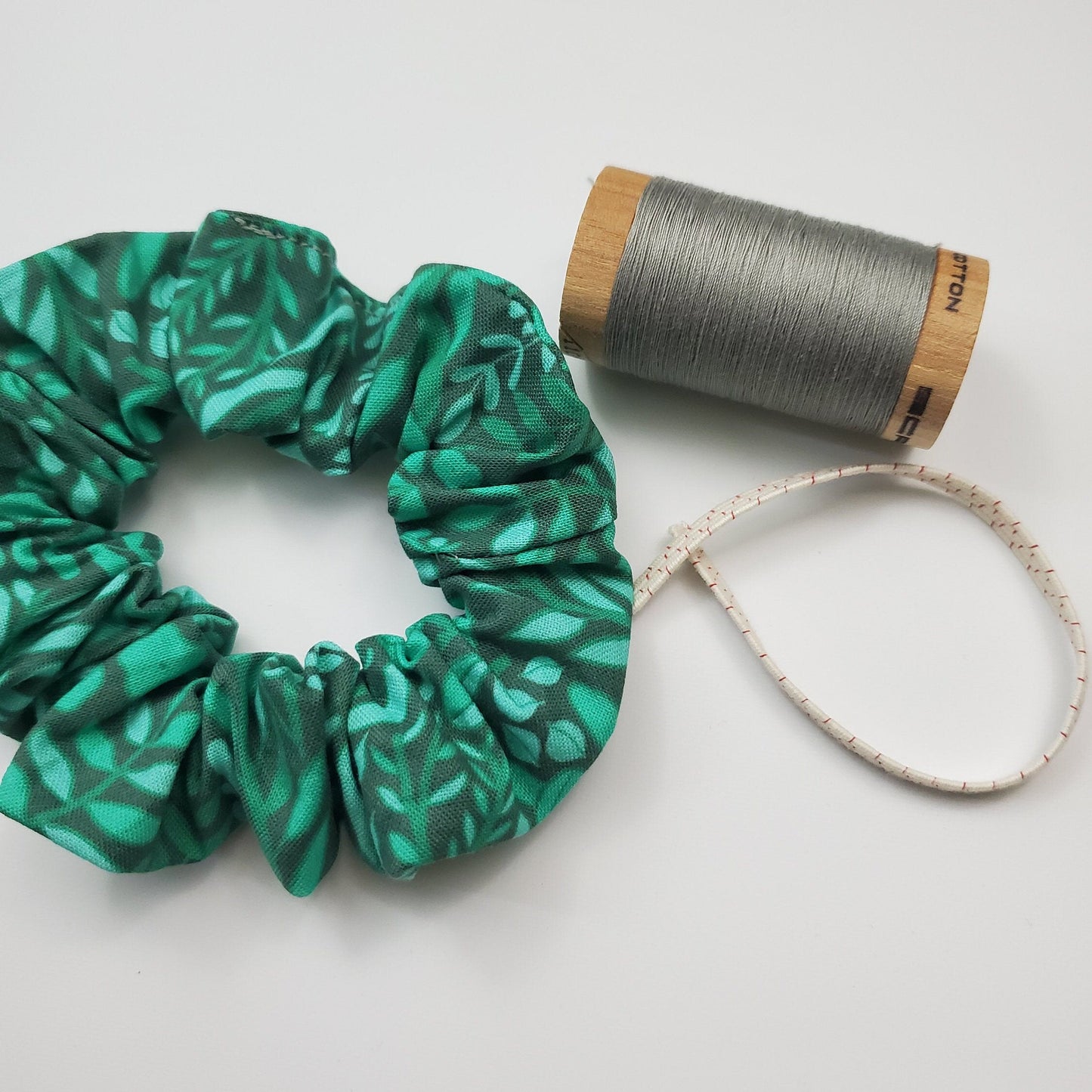 Scrunchie shown next to a wooden spool of grey thread, and a piece of the biodegradable elastic.
