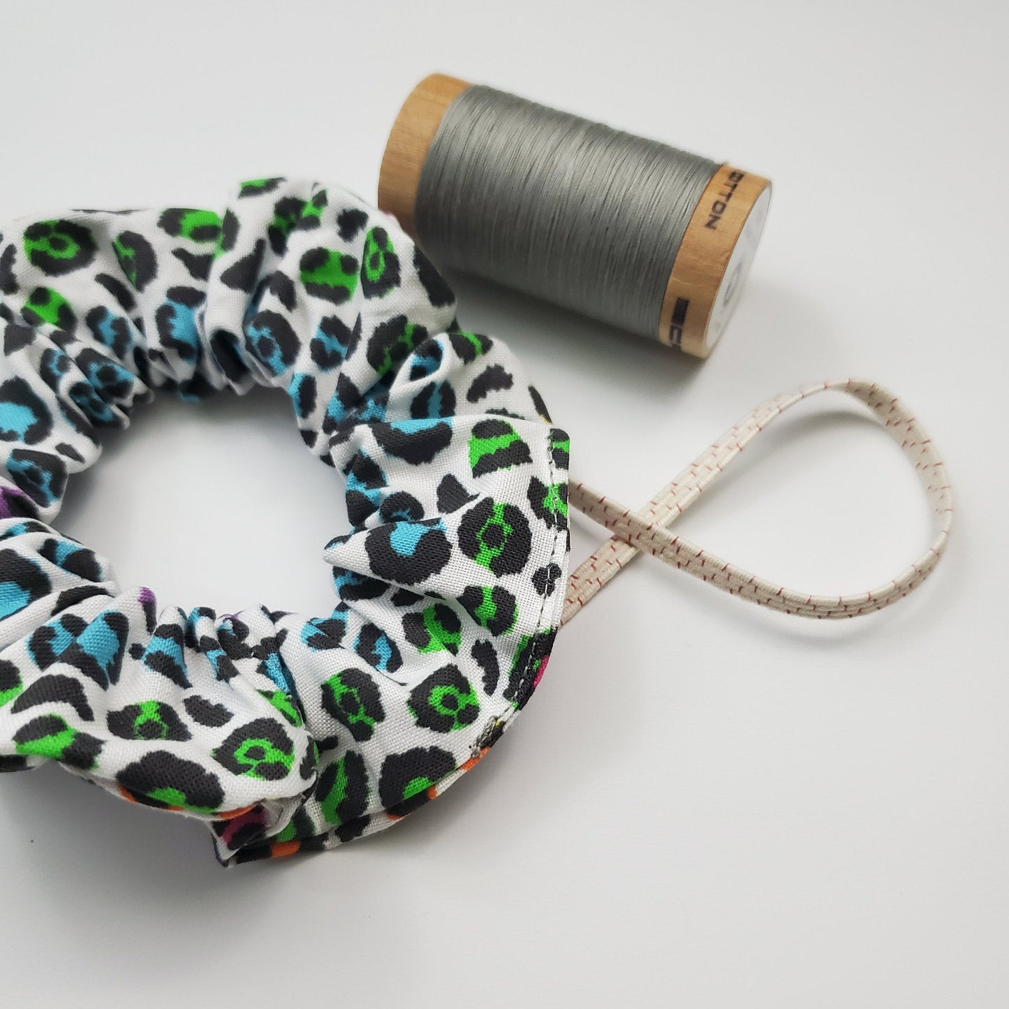 Scrunchie shown next to a wooden spool of grey thread, and a piece of the biodegradable elastic.