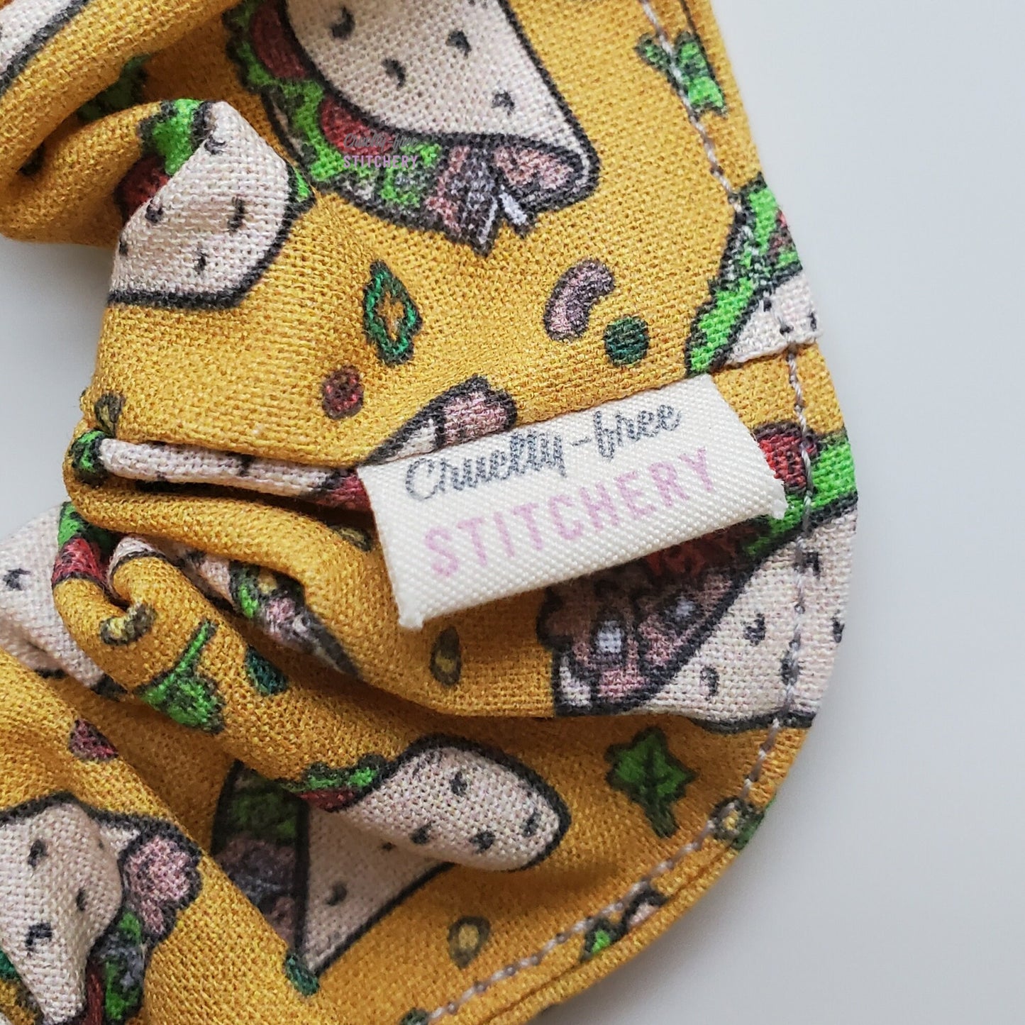 Close-up of the taco print scrunchie with a small white tag with the Cruelty-Free Stitchery logo.