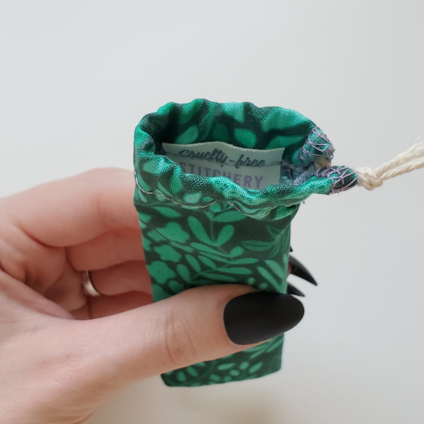 A reusable spork pouch, viewed from the top down. Inside the pouch is a tag with the Cruelty-Free Stitchery logo. The pouch is in someone's hand, the width is about half as wide as the thumb is long.