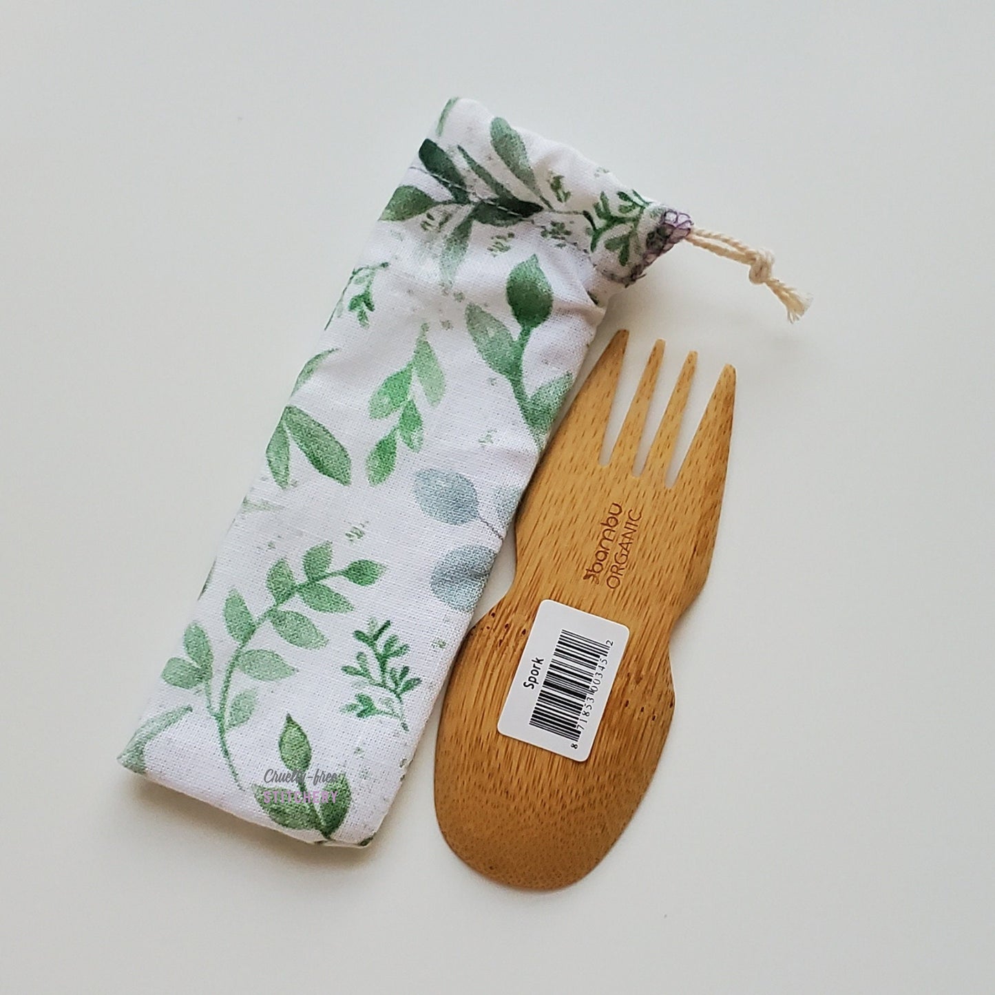 Reusable spork pouch laying diagonally next to an upside-down bamboo spork.
