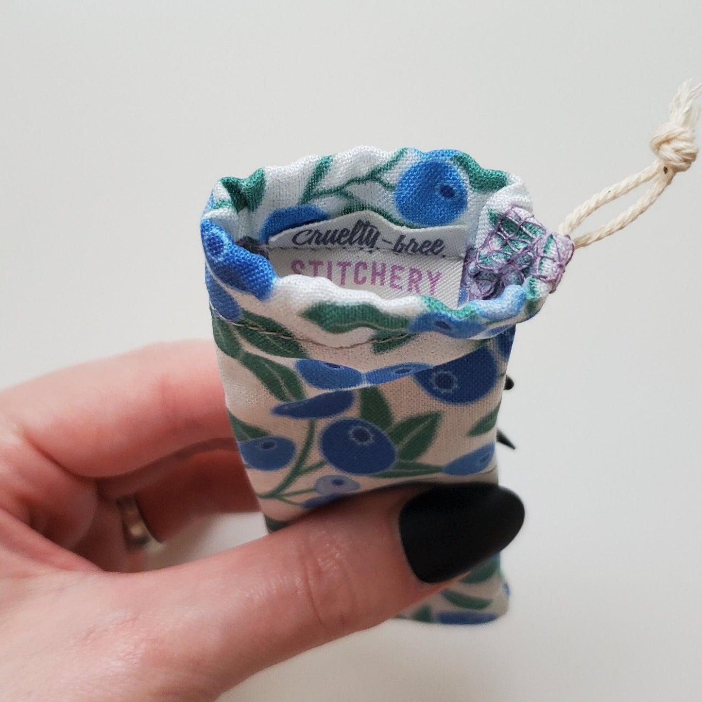 A reusable spork pouch, viewed from the top down. Inside the pouch is a tag with the Cruelty-Free Stitchery logo. The pouch is in someone's hand, the width is about half as wide as the thumb is long.