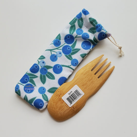 Reusable spork pouch laying diagonally next to an upside-down bamboo spork.