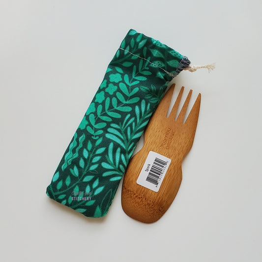 Reusable spork pouch laying diagonally next to an upside-down bamboo spork.