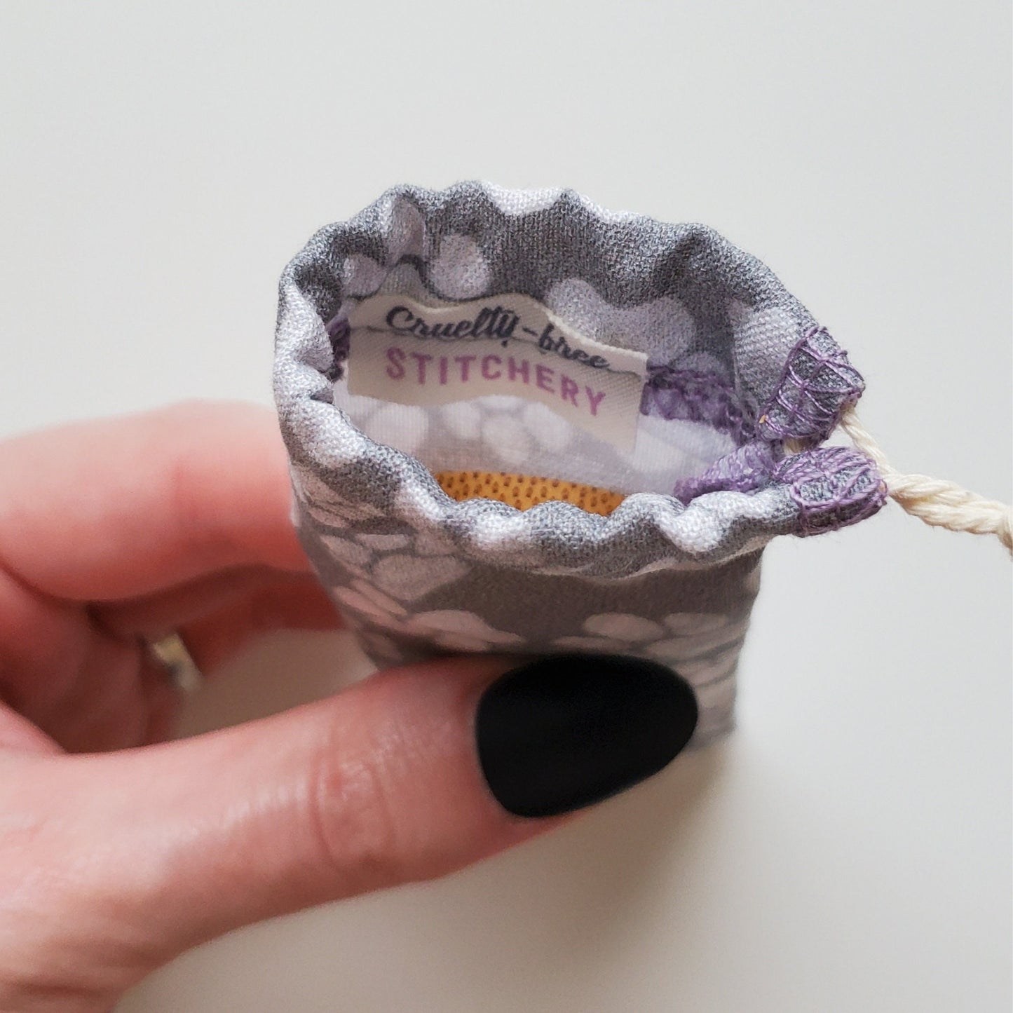 A reusable spork pouch, viewed from the top down. Inside the pouch is a tag with the Cruelty-Free Stitchery logo. The pouch is in someone's hand, the width is about half as wide as the thumb is long.