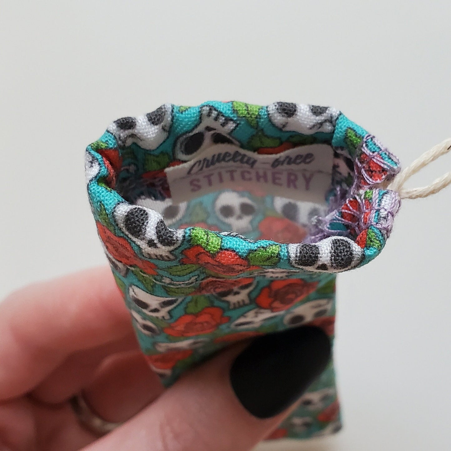 A reusable spork pouch, viewed from the top down. Inside the pouch is a tag with the Cruelty-Free Stitchery logo. The pouch is in someone's hand, the width is about half as wide as the thumb is long.