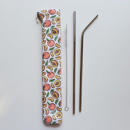 Reusable straw pouch in the same peach print laying vertically next to a straw cleaner brush, a straight stainless steel straw, and a bent stainless steel straw.
