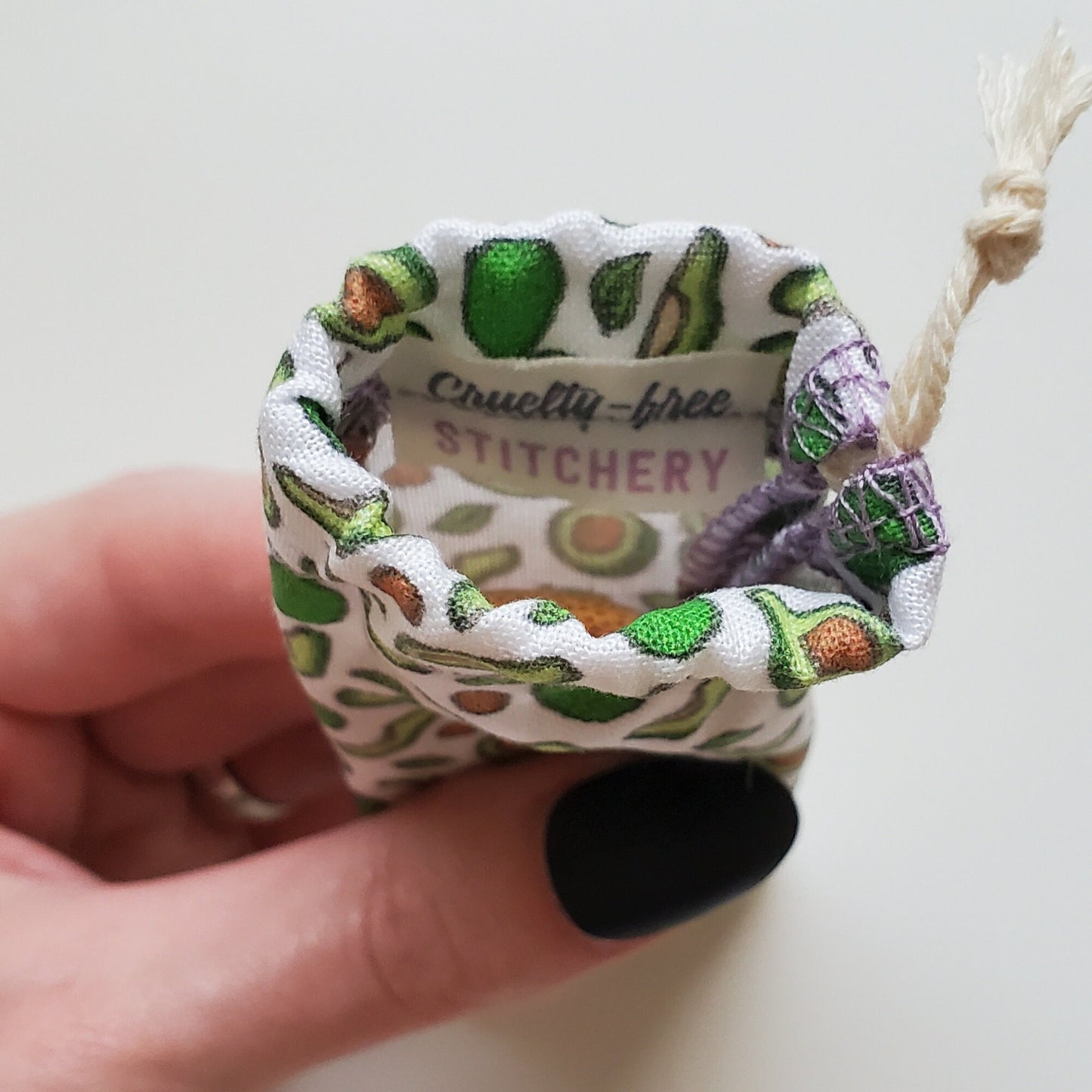 A reusable spork pouch, viewed from the top down. Inside the pouch is a tag with the Cruelty-Free Stitchery logo. The pouch is in someone's hand, the width is about half as wide as the thumb is long.