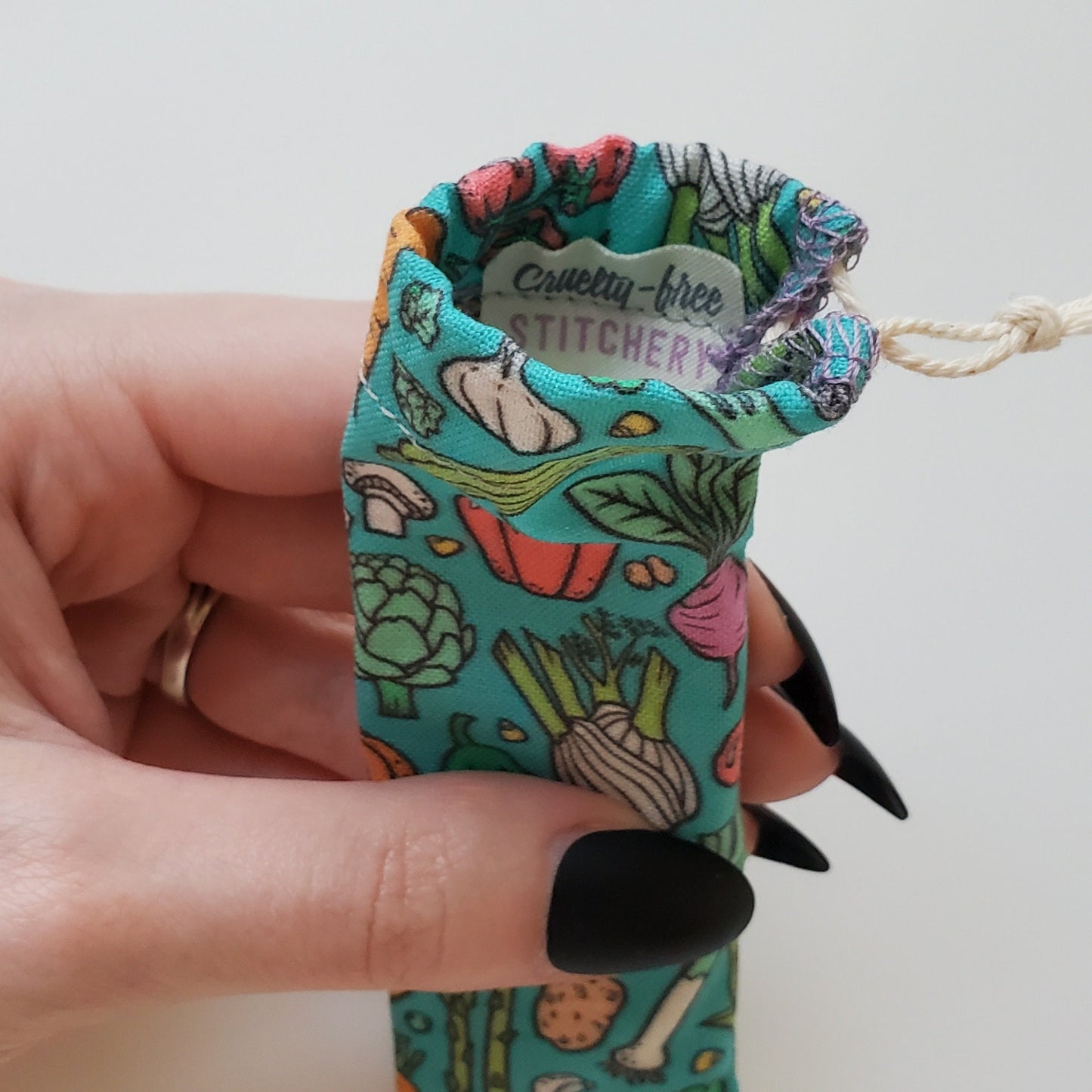 A reusable spork pouch, viewed from the top down. Inside the pouch is a tag with the Cruelty-Free Stitchery logo. The pouch is in someone's hand, the width is about half as wide as the thumb is long.