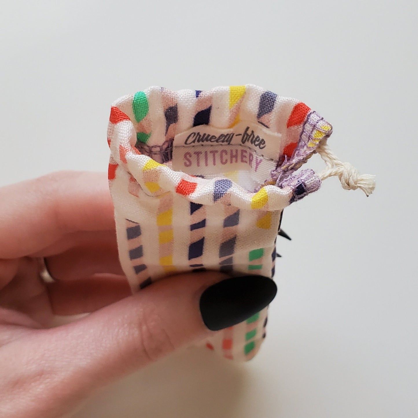 A reusable spork pouch, viewed from the top down. Inside the pouch is a tag with the Cruelty-Free Stitchery logo. The pouch is in someone's hand, the width is about half as wide as the thumb is long.