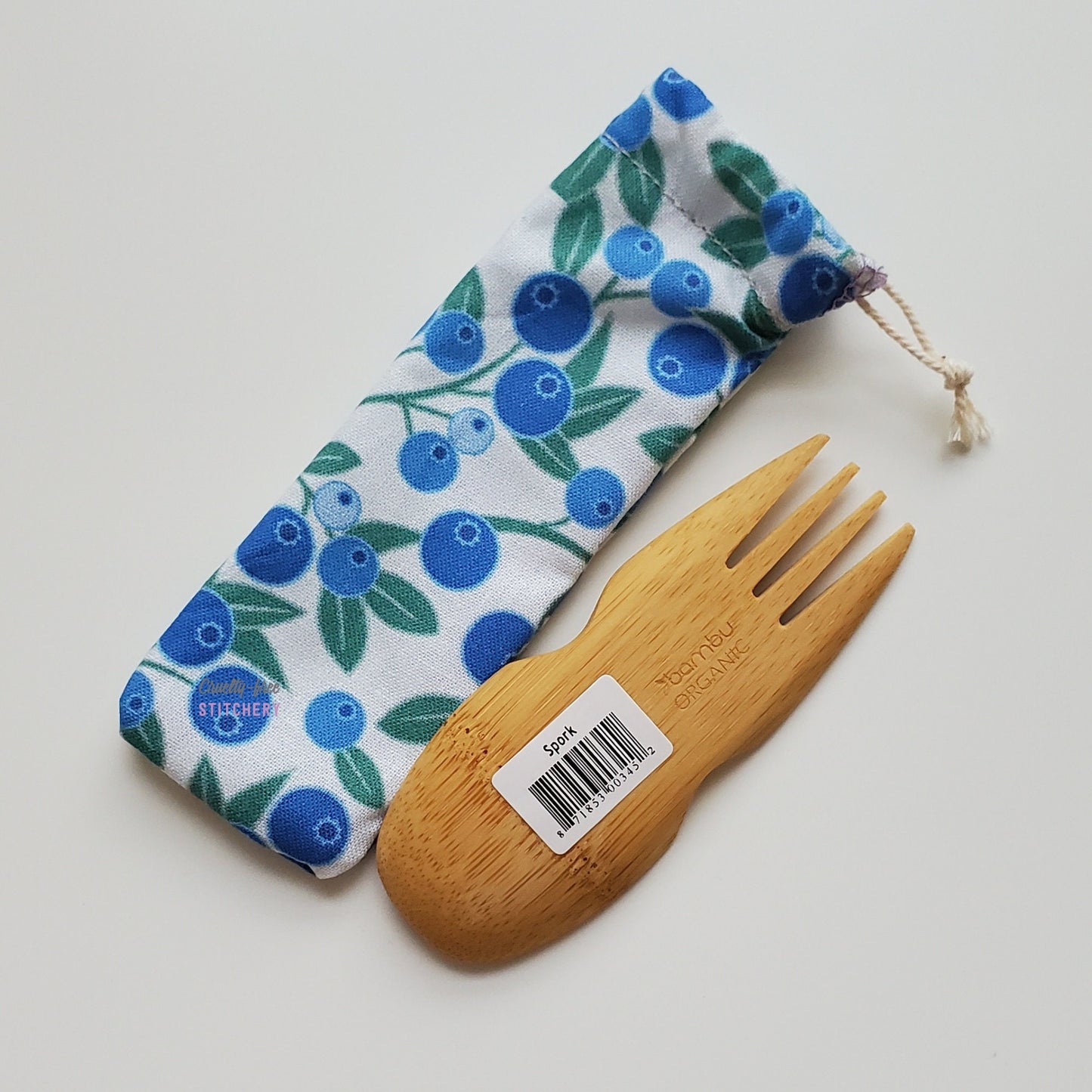 Reusable spork pouch with a blueberry print fabric. The bamboo spork is laid upside-down next to the pouch.