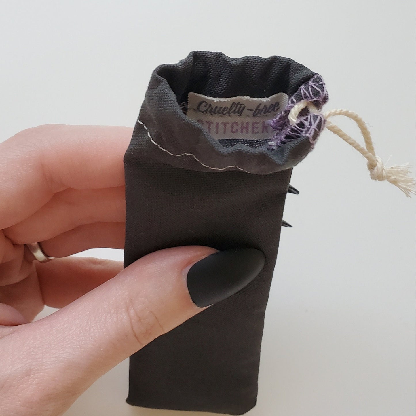A reusable spork pouch, viewed from the top down. Inside the pouch is a tag with the Cruelty-Free Stitchery logo. The pouch is in someone's hand, the width is about half as wide as the thumb is long.