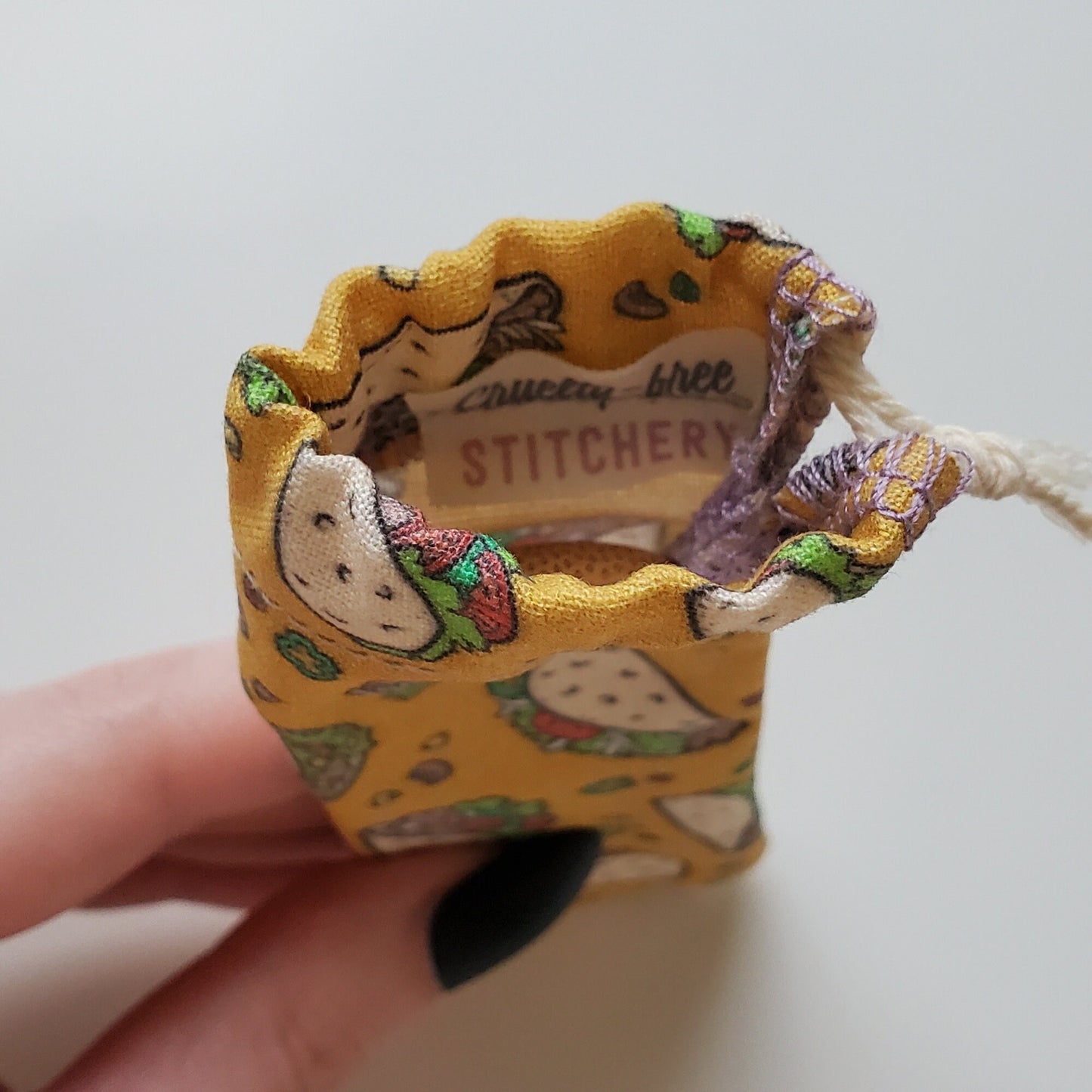 A reusable spork pouch, viewed from the top down. Inside the pouch is a tag with the Cruelty-Free Stitchery logo. The pouch is in someone's hand, the width is about half as wide as the thumb is long.