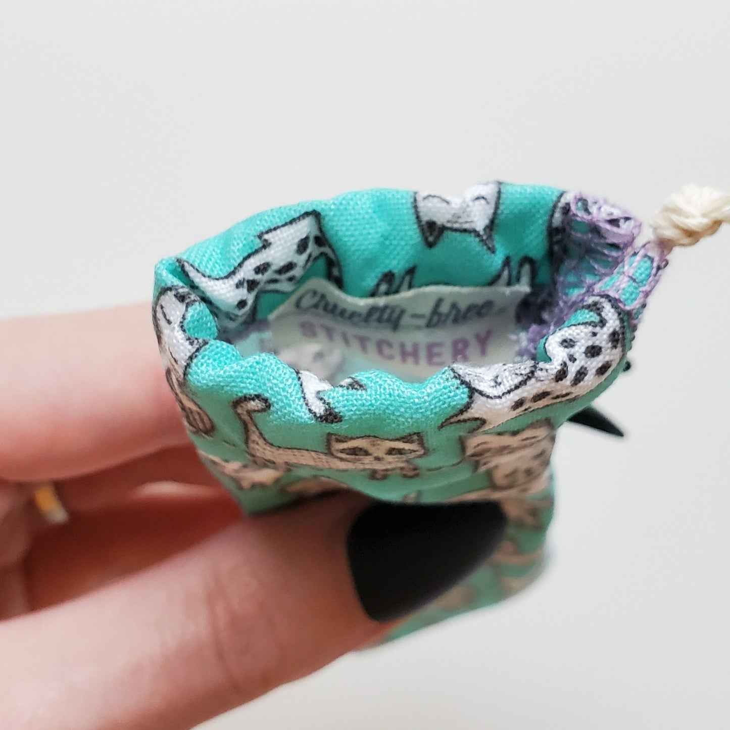 A reusable spork pouch, viewed from the top down. Inside the pouch is a tag with the Cruelty-Free Stitchery logo. The pouch is in someone's hand, the width is about half as wide as the thumb is long.