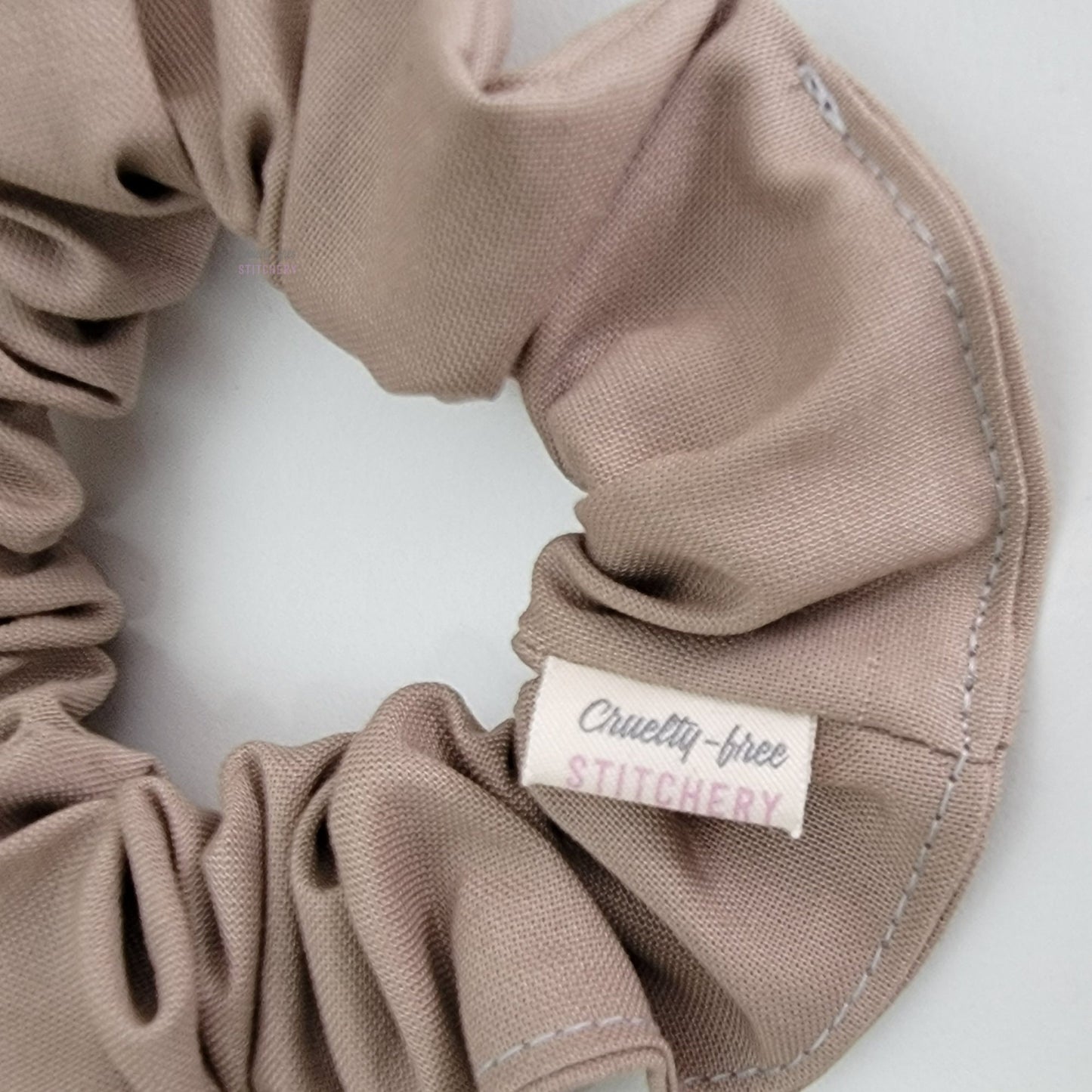 Close-up of the scrunchie, with a small white tag with the Cruelty-Free Stitchery logo.