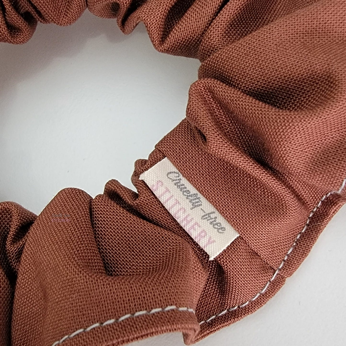 Close-up of the scrunchie with a small white tag with the Cruelty-Free Stitchery logo.