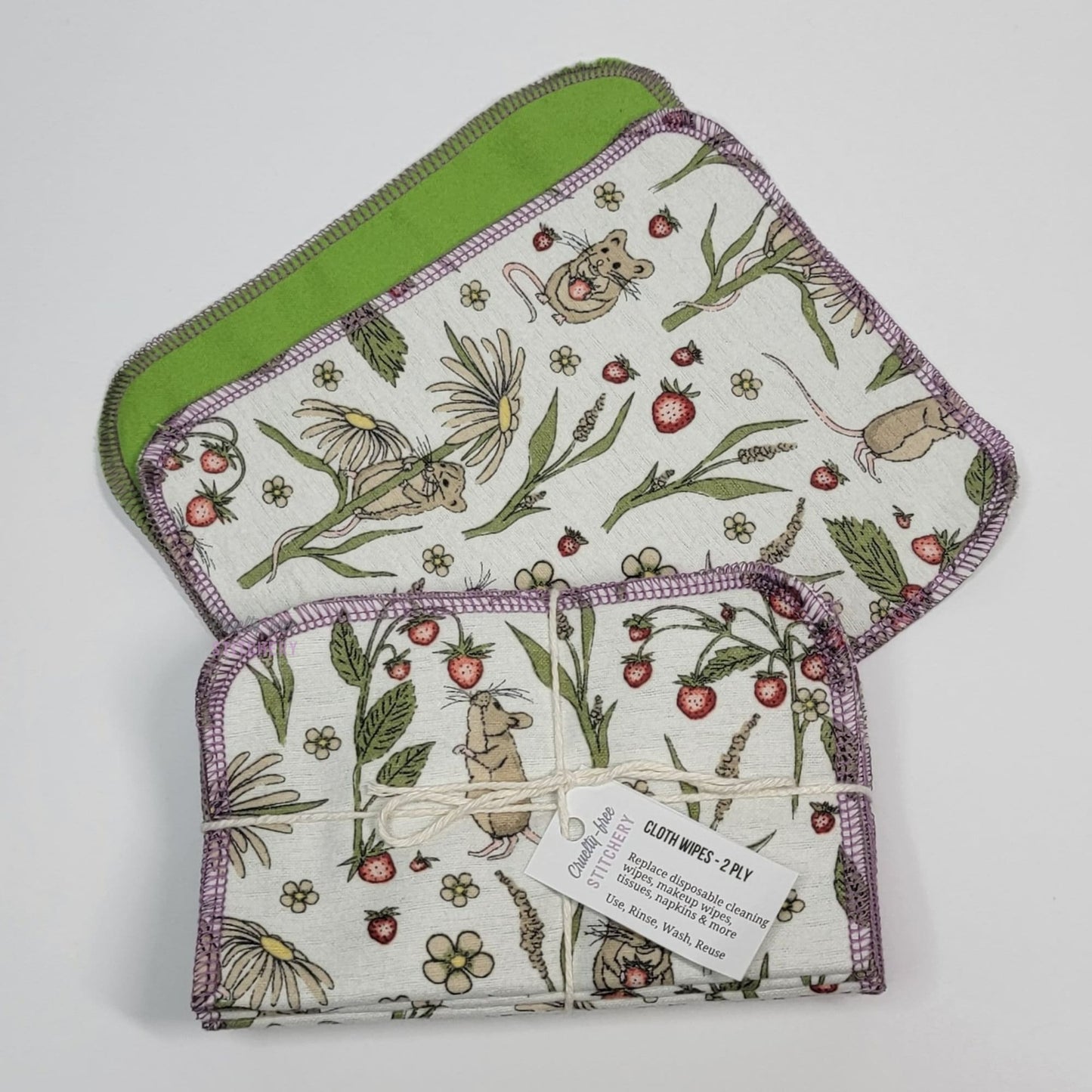 A front and back of the mouse cloth wipes, next to a bundled pack of the wipes. The bundle is tied with a string and a small paper tag.