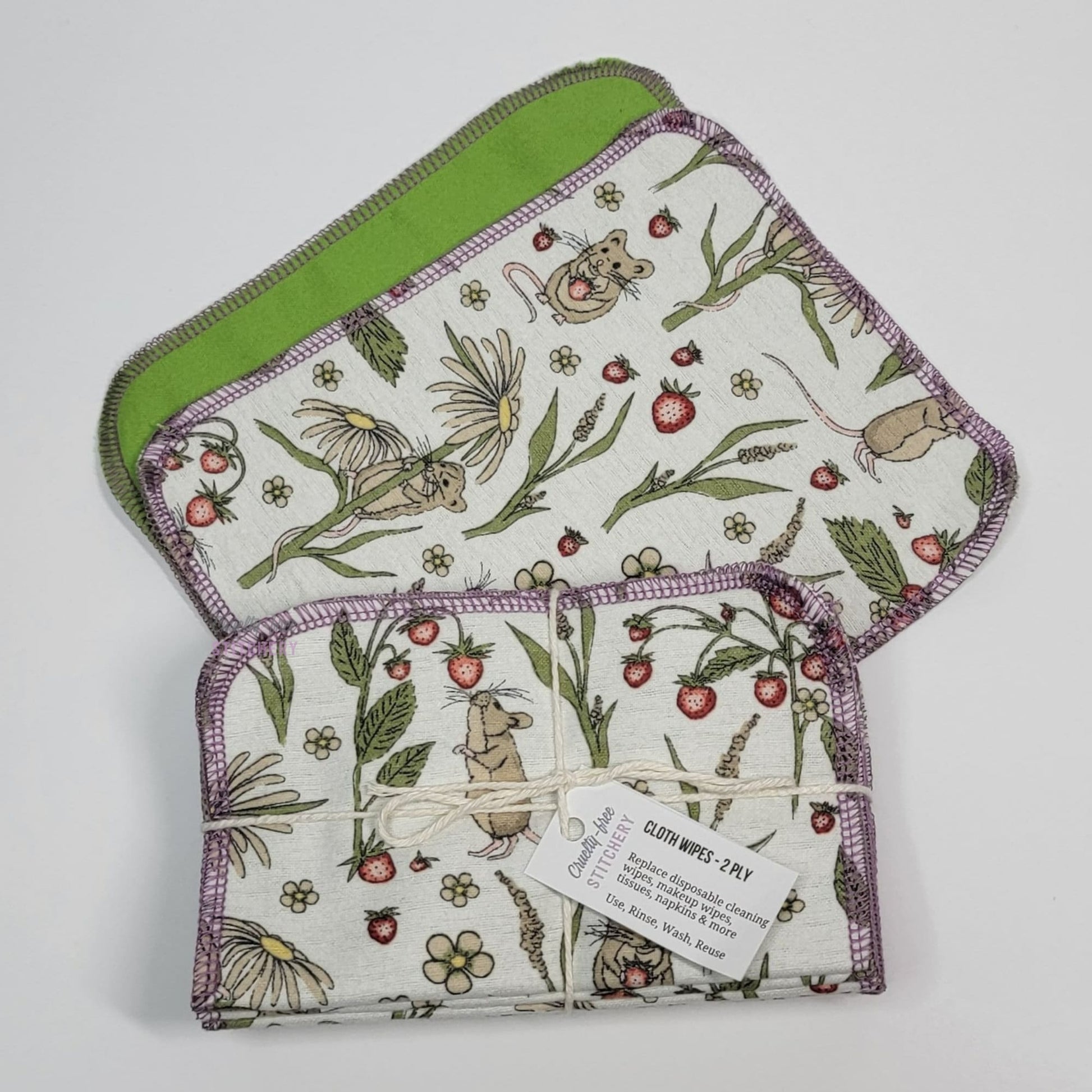 A front and back of the mouse cloth wipes, next to a bundled pack of the wipes. The bundle is tied with a string and a small paper tag.