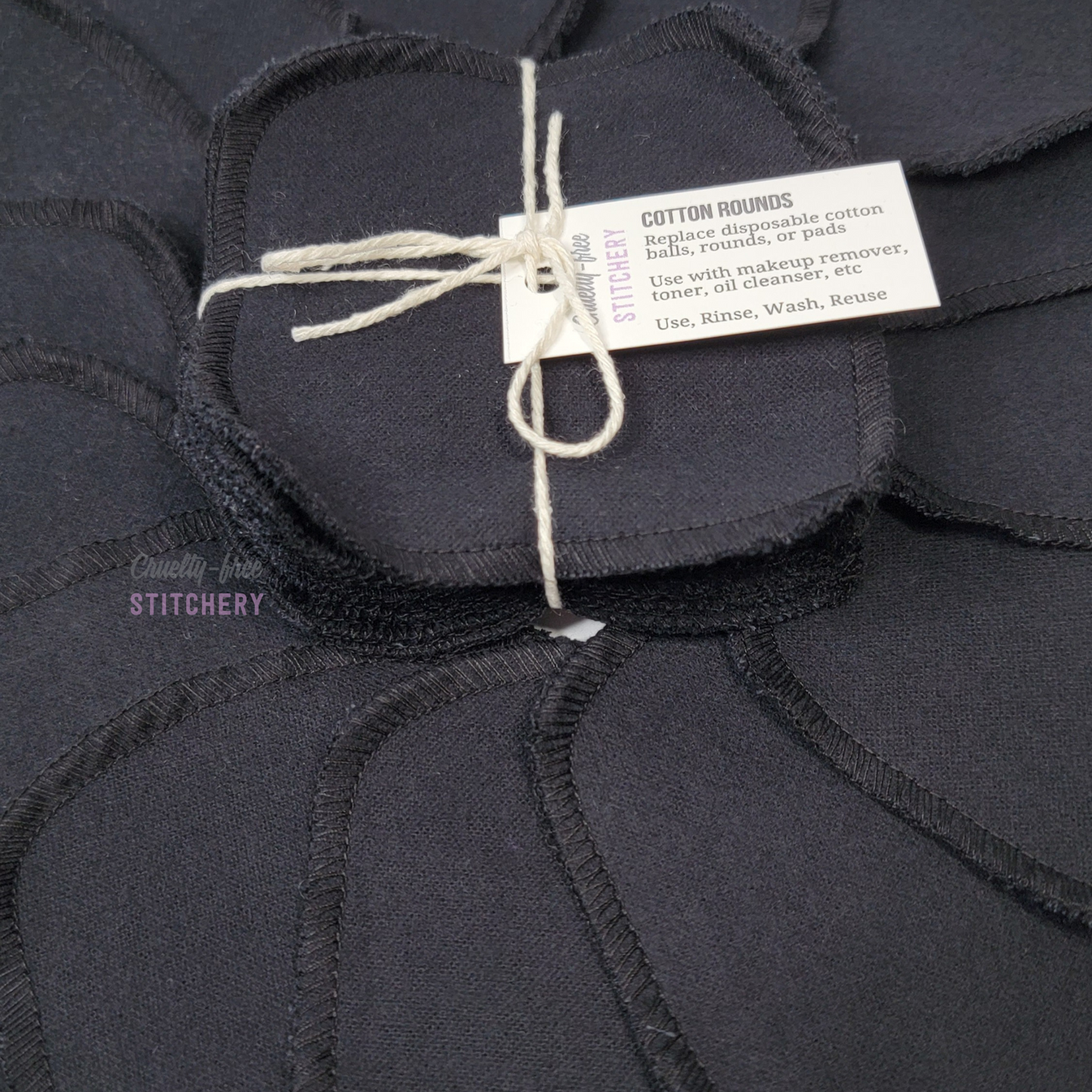 Close-up of the black reusable cotton rounds. They are a rounded square shape.