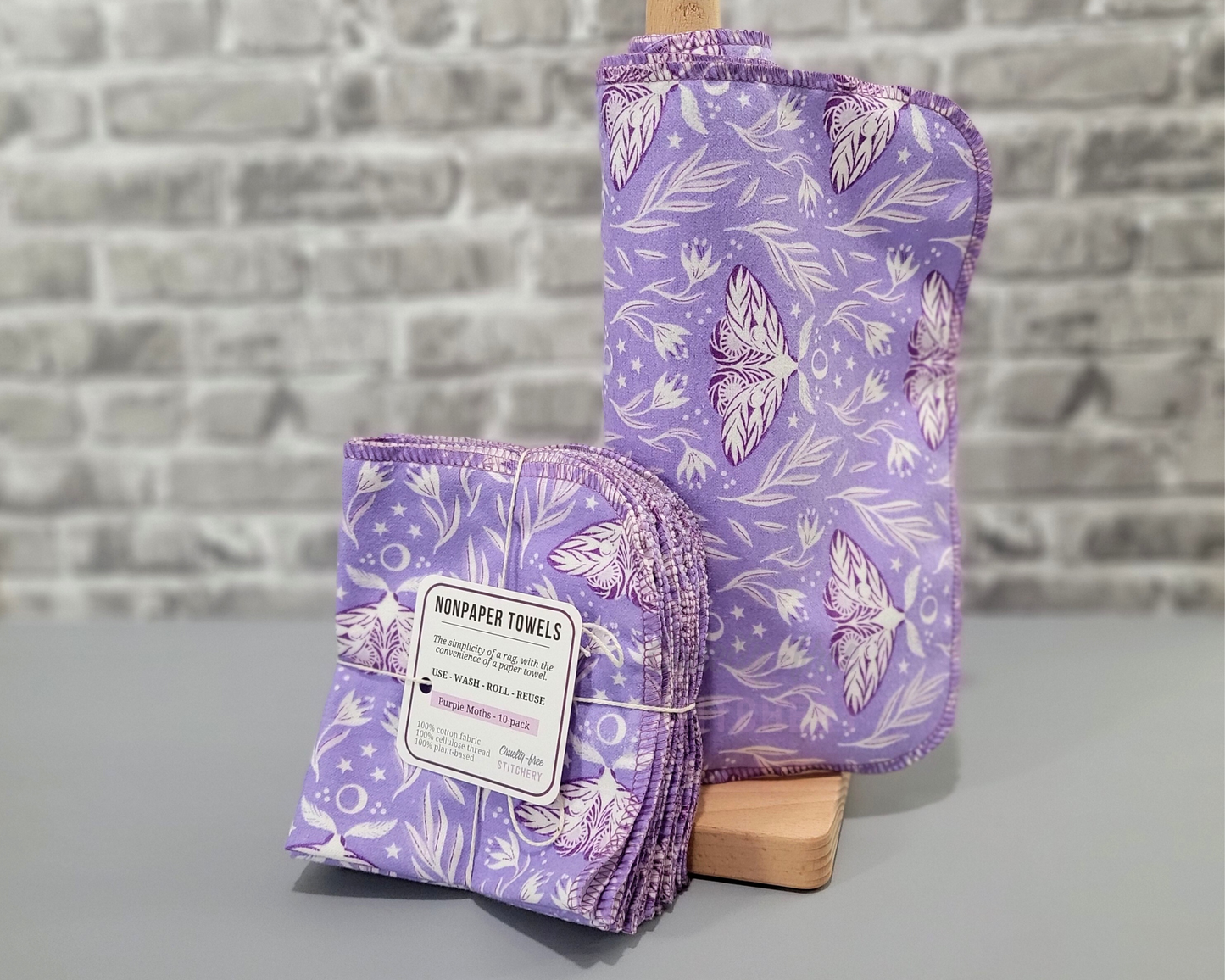 Purple Moths NonPaper Towels. A roll of light purple cloths with darker purple moths and ethereal floral design, next to a bundled pack.